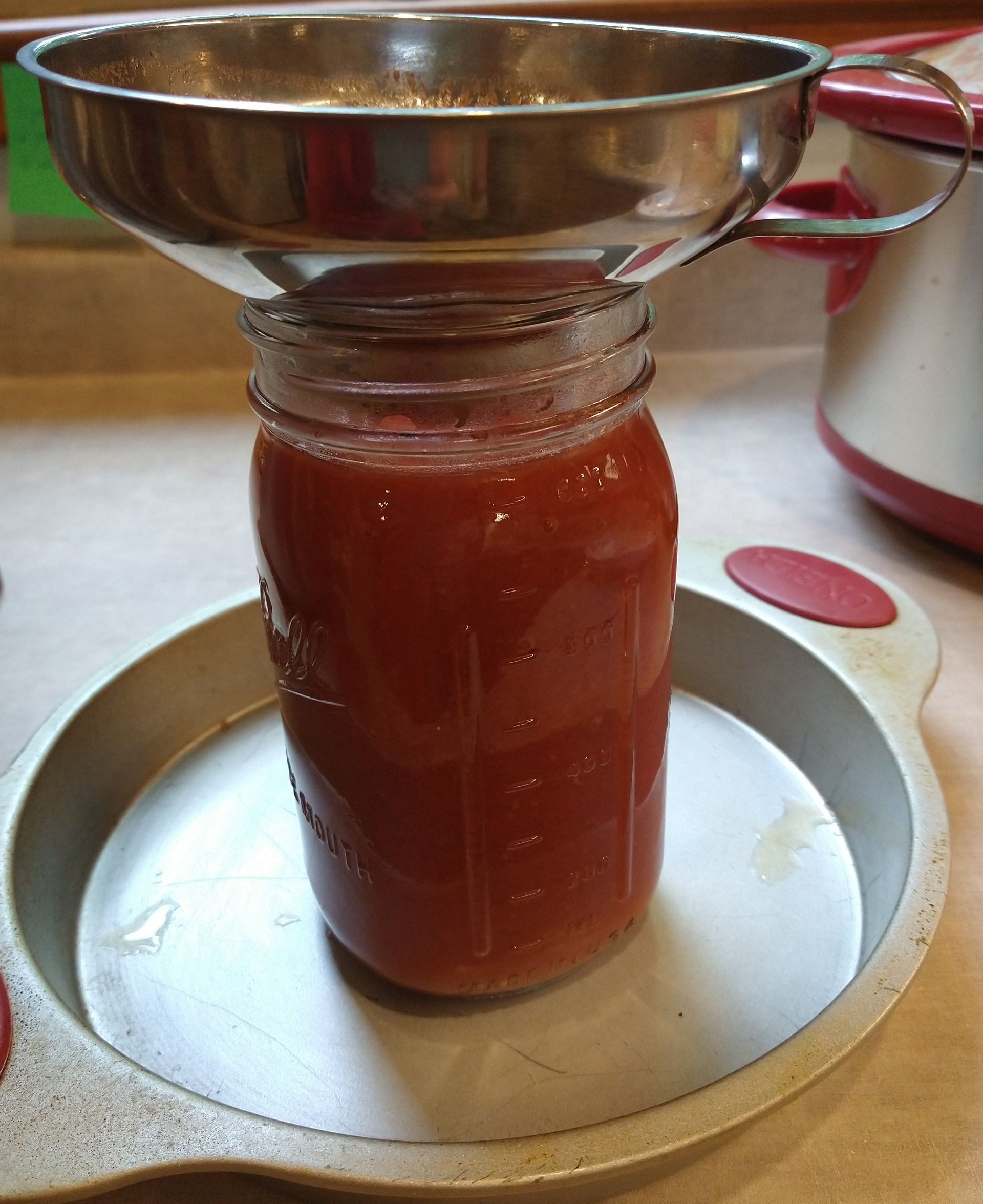 Photo of a jar filled with thick tomato sauce with a canning funnel on top