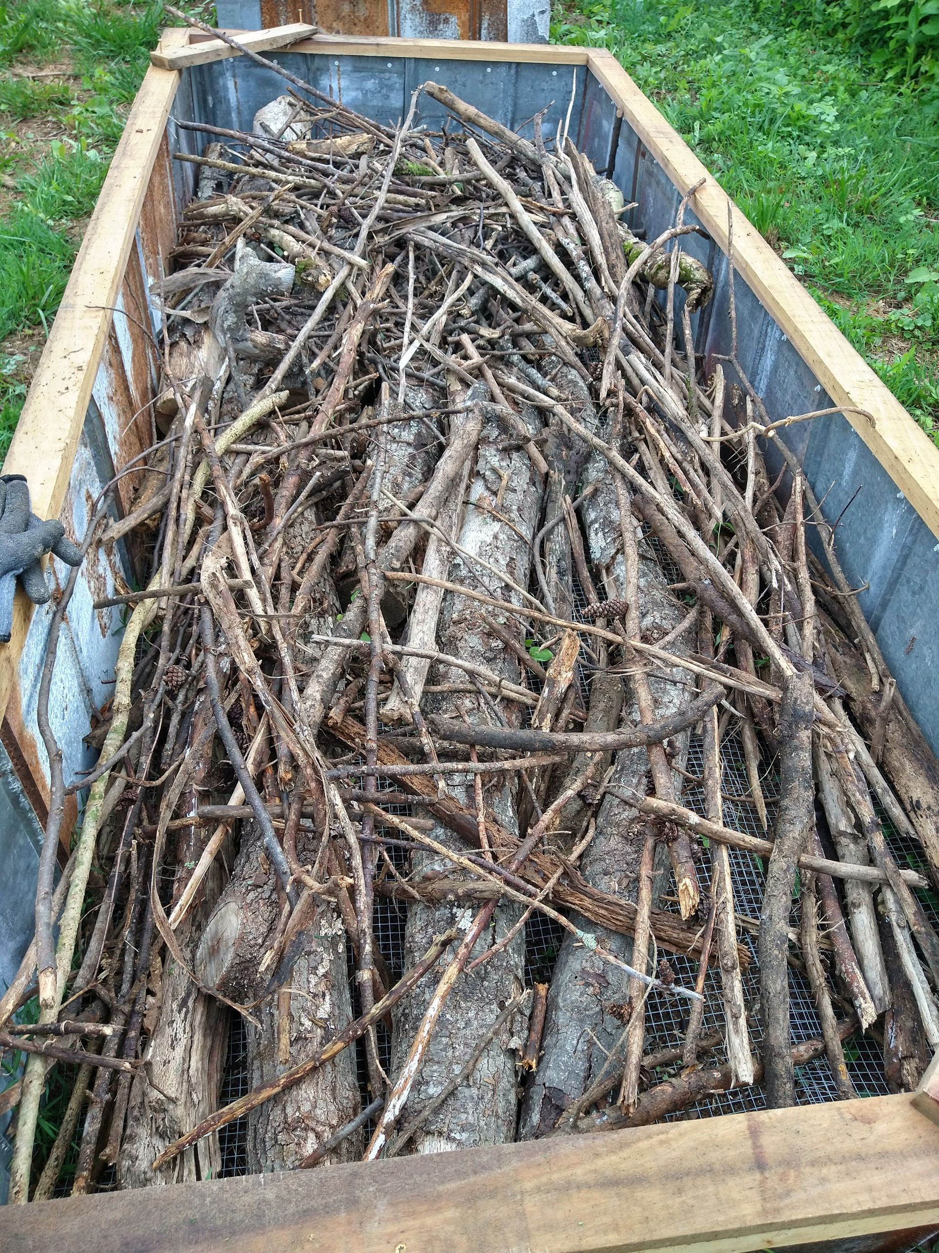 A close-up of smaller sticks being placed in bed to raise the level of the Hugelkultur because most plants will not need more than 18