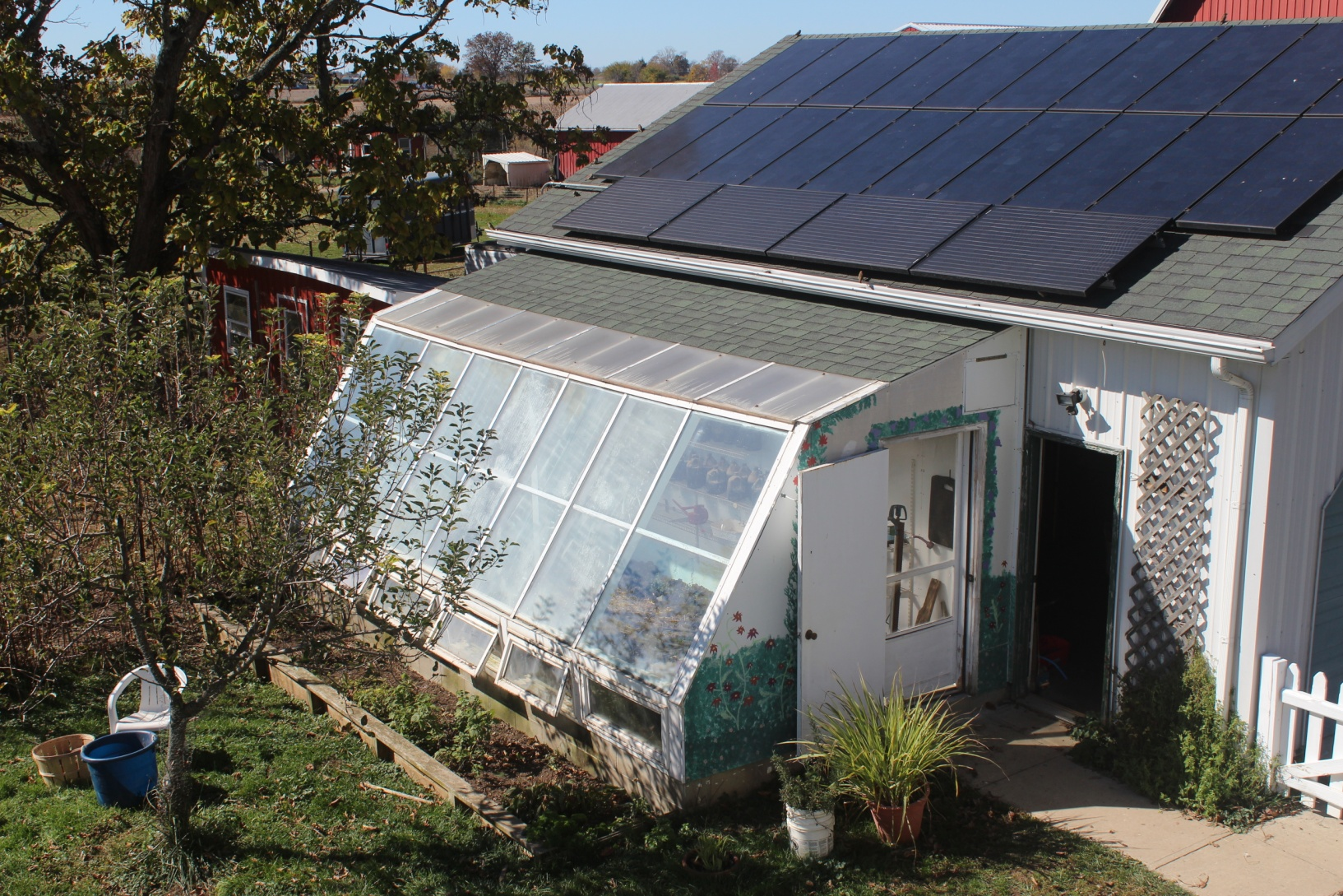 Looking down on a lean-to greenhouse in summer attached to a garage with solar panels