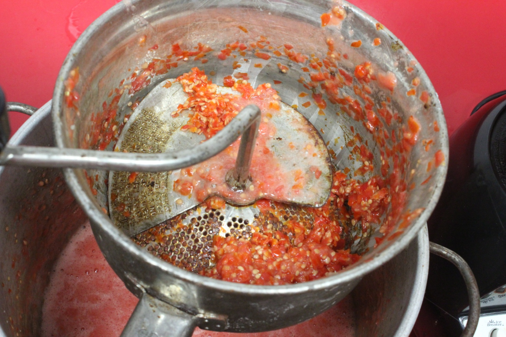 Photo of the food mill containing only the skin and seeds of the tomatoes after the juice has been spun into the pot below
