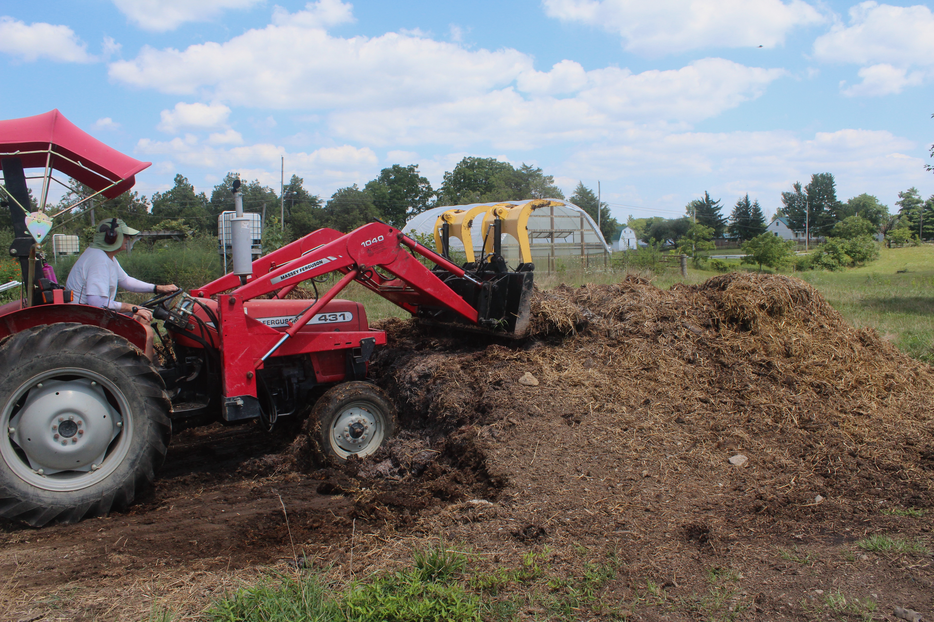 Photo of red tractor turning a pile of compost with a hoop house in the background