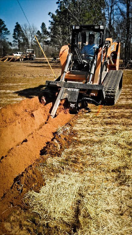 Orange trackhoe digging a trench in a field.  A person operates the machine.  Sunlight illuminates the scene.