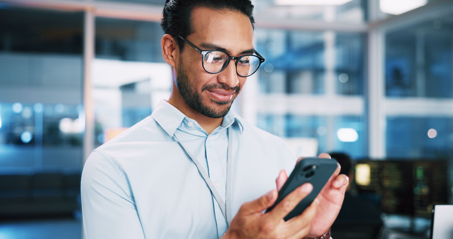 Man in glasses using a smartphone in a modern office setting