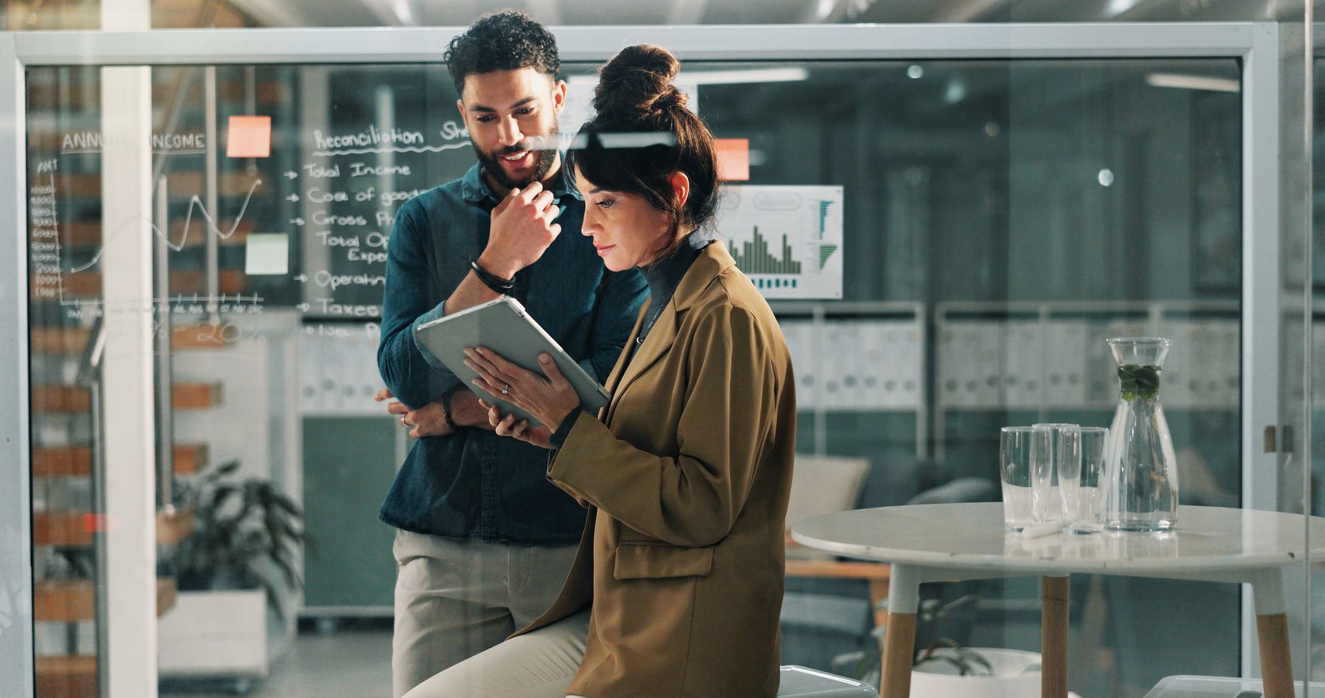 Two people reviewing a tablet in a modern glass-walled office