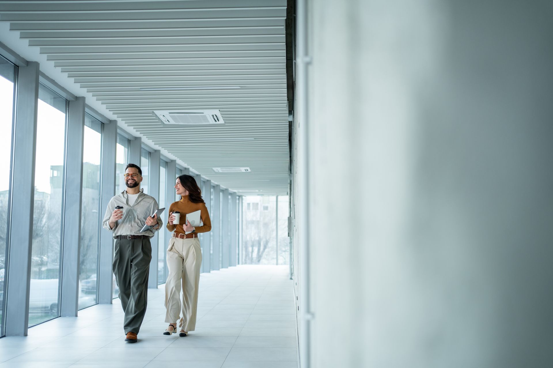 Two people walking and talking in a bright, modern hallway with glass walls