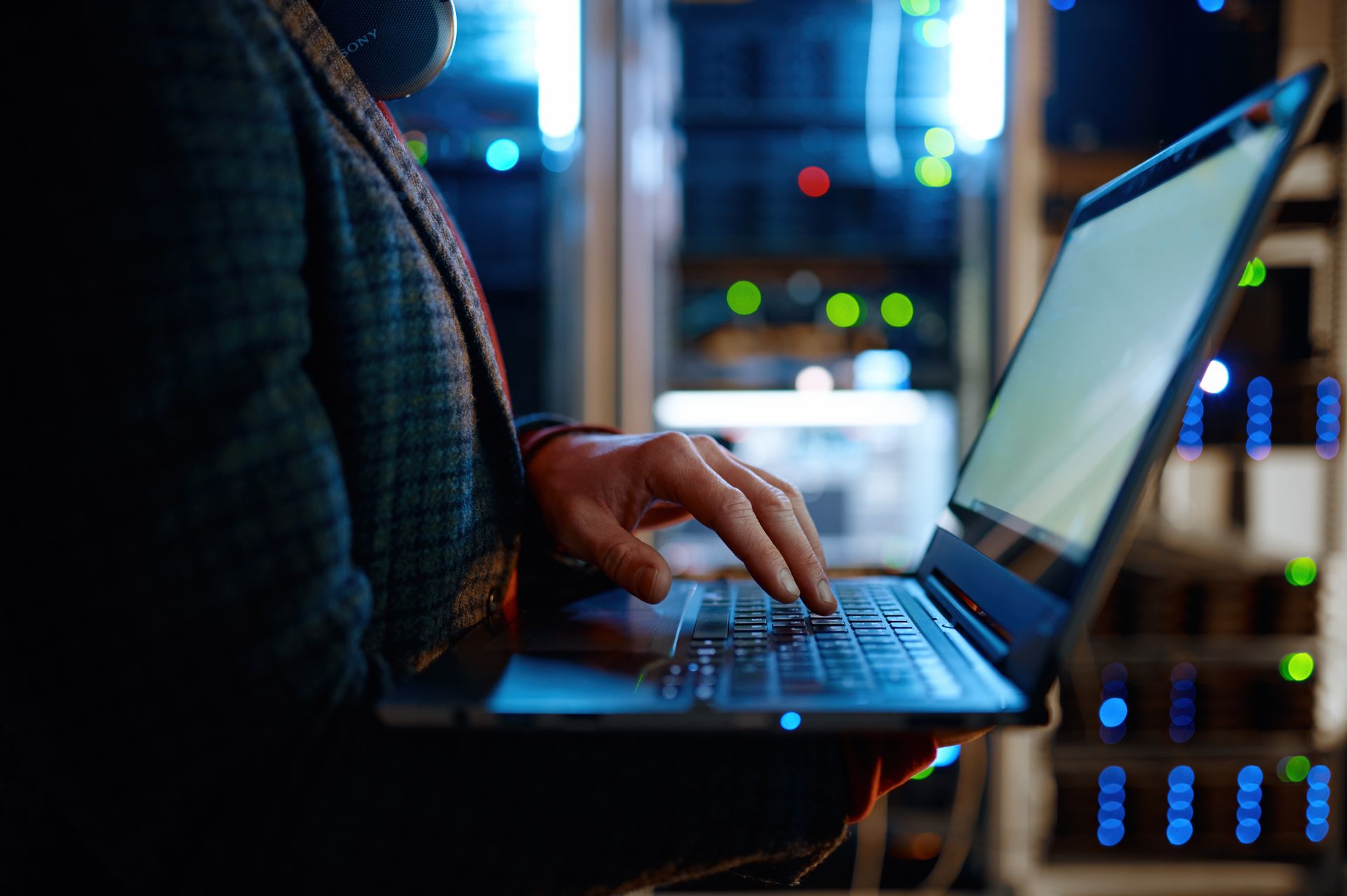 Person typing on a laptop in a server room with glowing rack lights
