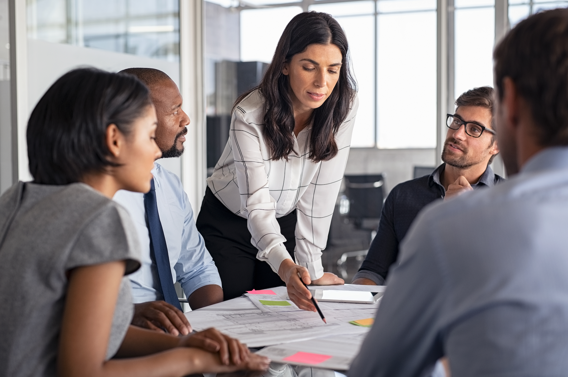 Team meeting around a table as a woman in a white blouse reviews documents with colleagues