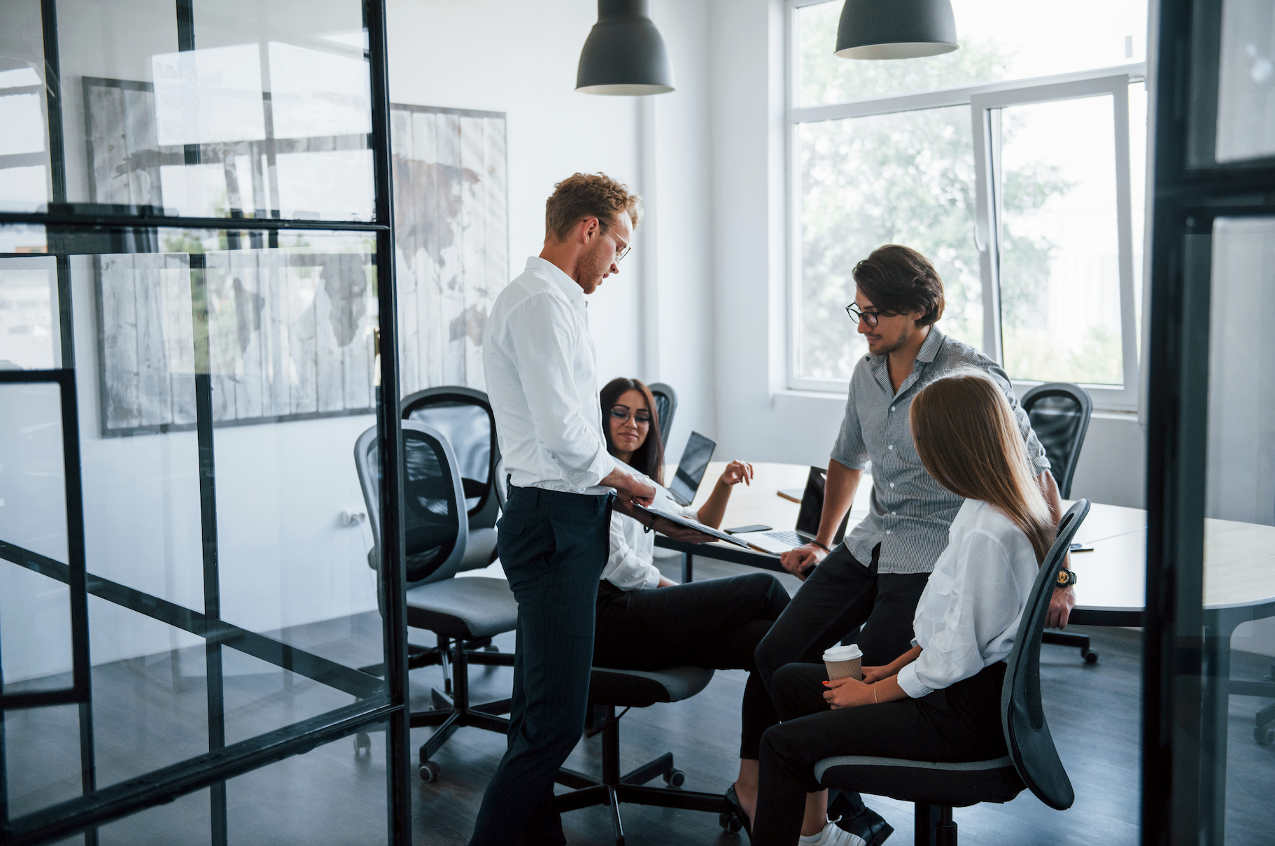 Coworkers in a bright modern office meeting around a desk with laptops and papers