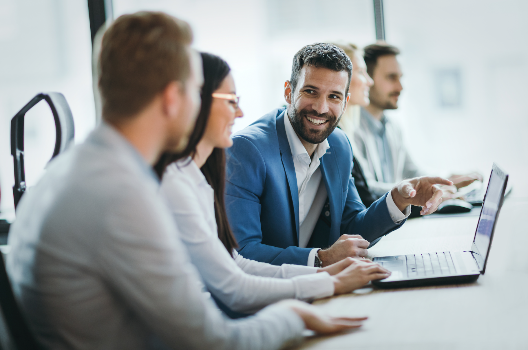 Colleagues in a meeting, smiling and talking around a laptop in a bright office