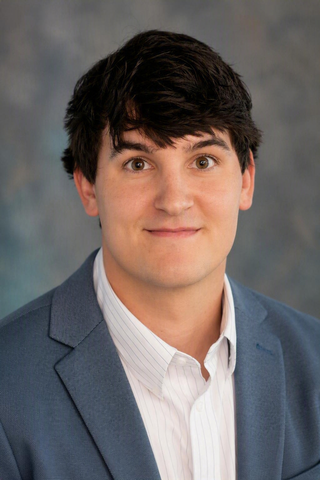 Portrait of a person in a blue blazer and white shirt against a gray studio backdrop