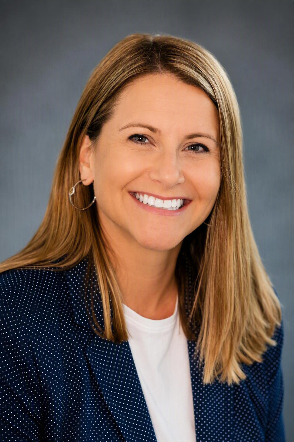 Smiling woman in navy blazer and white top against a gray background