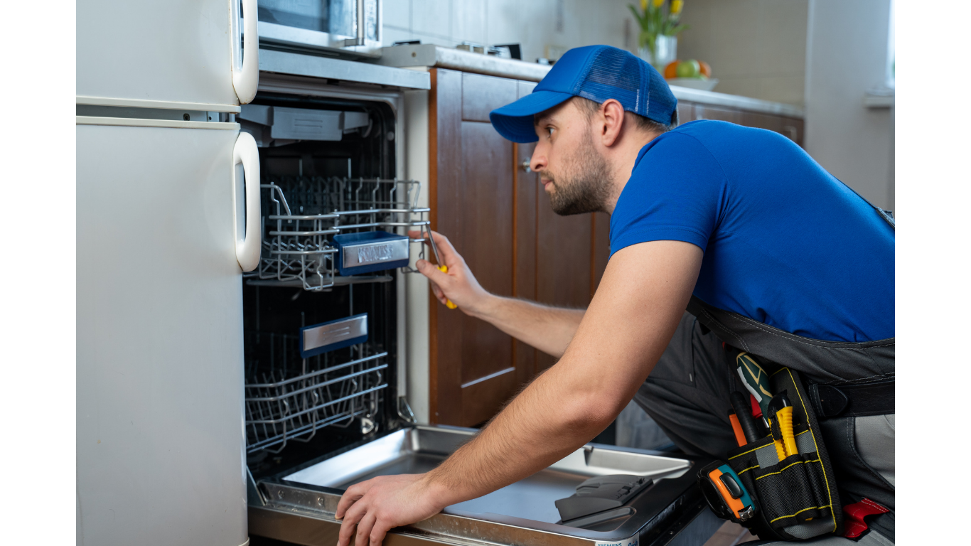 Refrigerator repairman in blue overalls, inspecting the open refrigerator door in a kitchen.