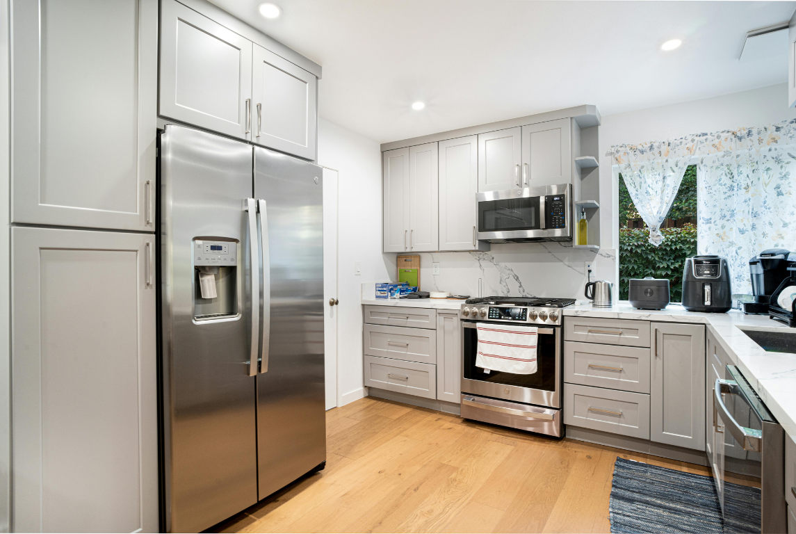 Gray kitchen with stainless steel appliances, light wood floors, and white countertops.