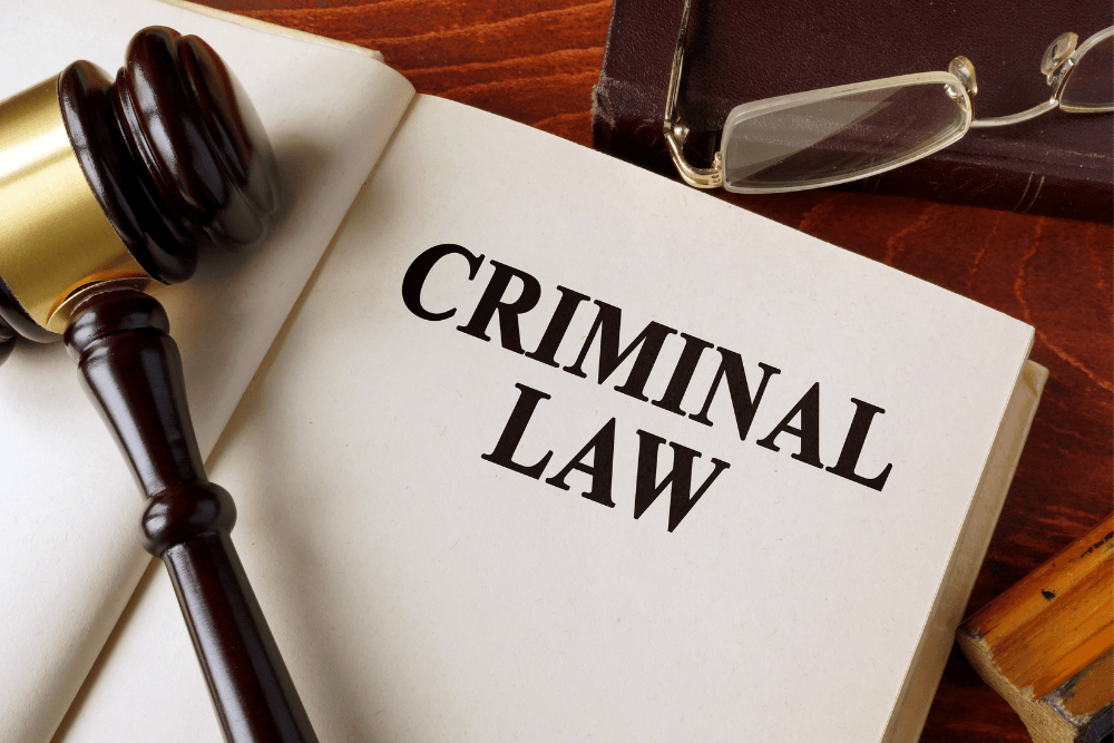 Criminal law book beside a judge’s gavel and eyeglasses on a wooden desk