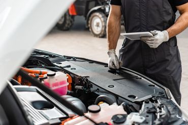 Mechanic in gloves inspecting car engine with hood open in a garage