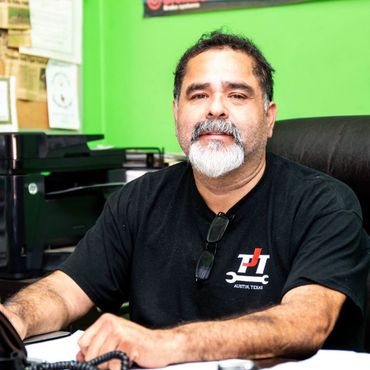 Man seated at a desk in a bright green office, wearing a black T-shirt and looking at the camera.