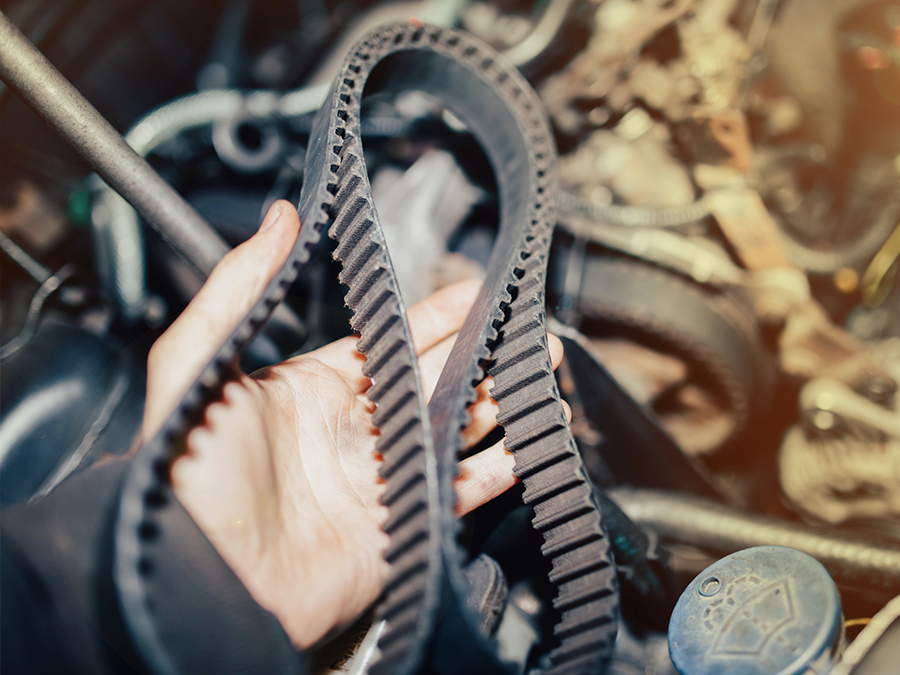 Hand holding a black toothed rubber belt among car parts and cables