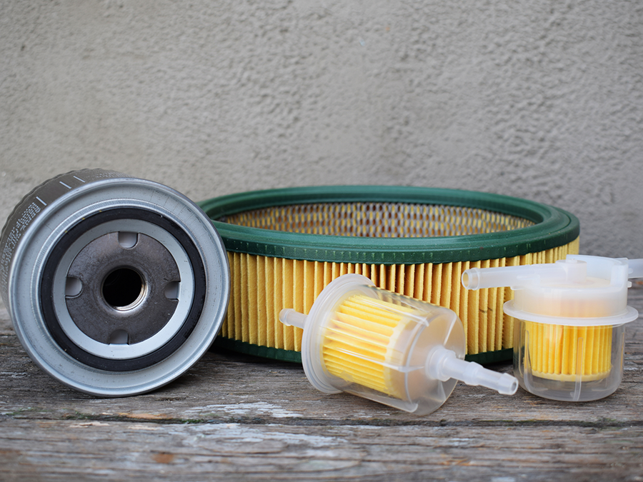 Set of automotive oil filters on weathered wood, with one metal filter and three yellow pleated filters.