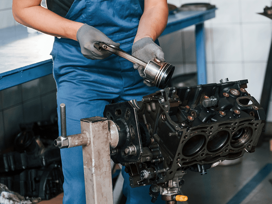 Mechanic in blue overalls working on an engine block in a workshop