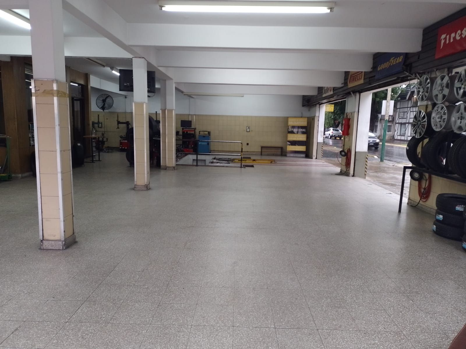 Local comercial o garaje vacío con suelo de hormigón, pilares y neumáticos expuestos a lo largo de la pared derecha.