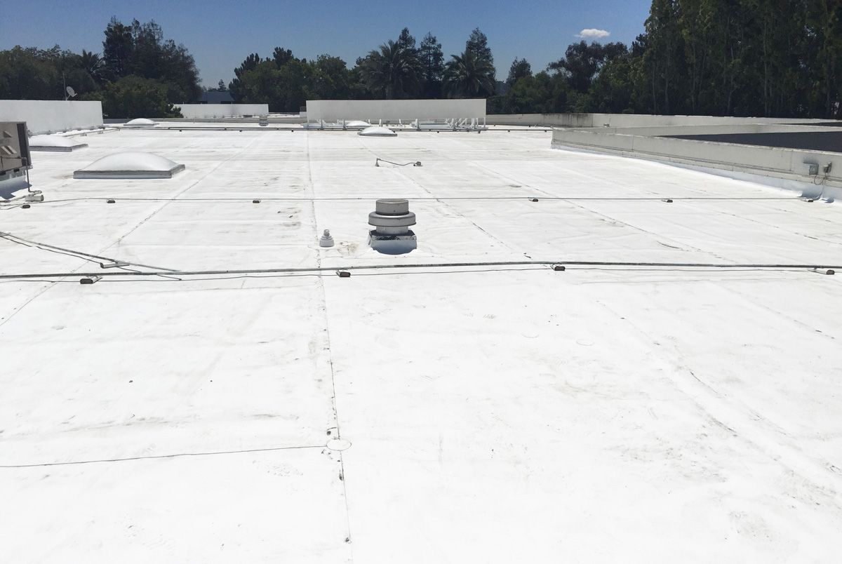 The roof of a building with a white roof and trees in the background.