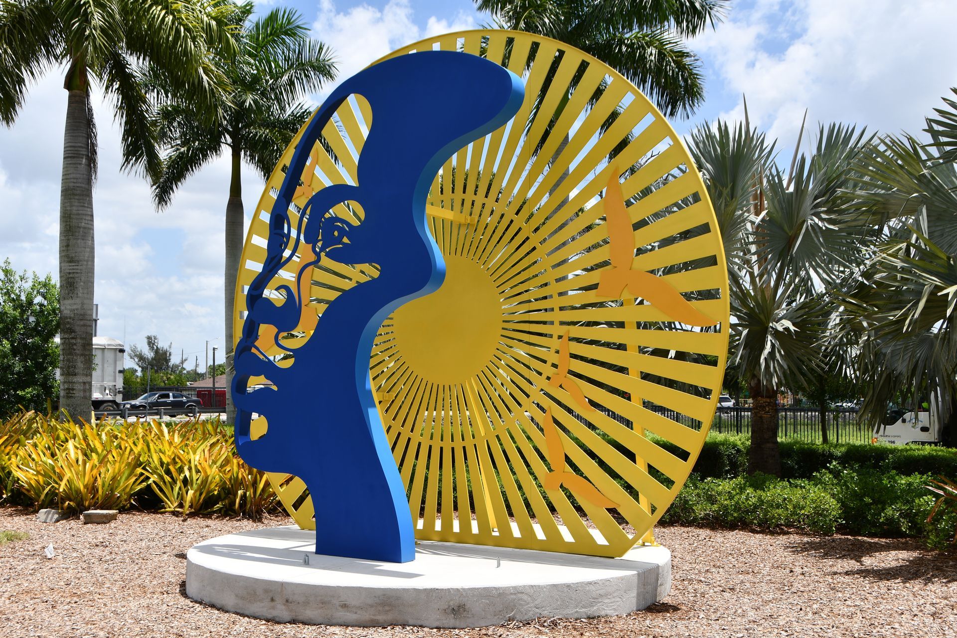 A blue and yellow sculpture in a park with palm trees in the background