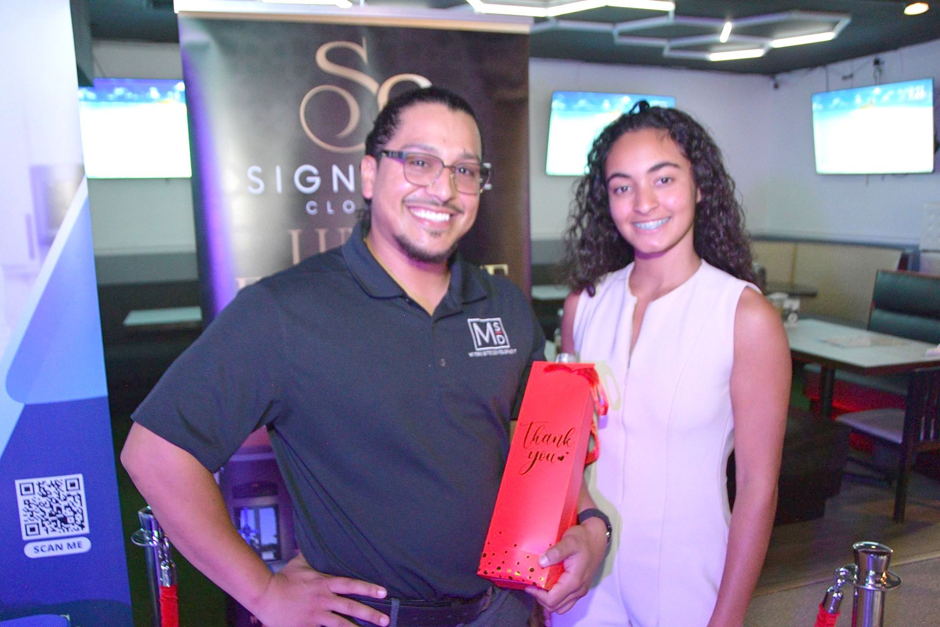 A man and a woman standing next to each other holding a red bag that says thank you