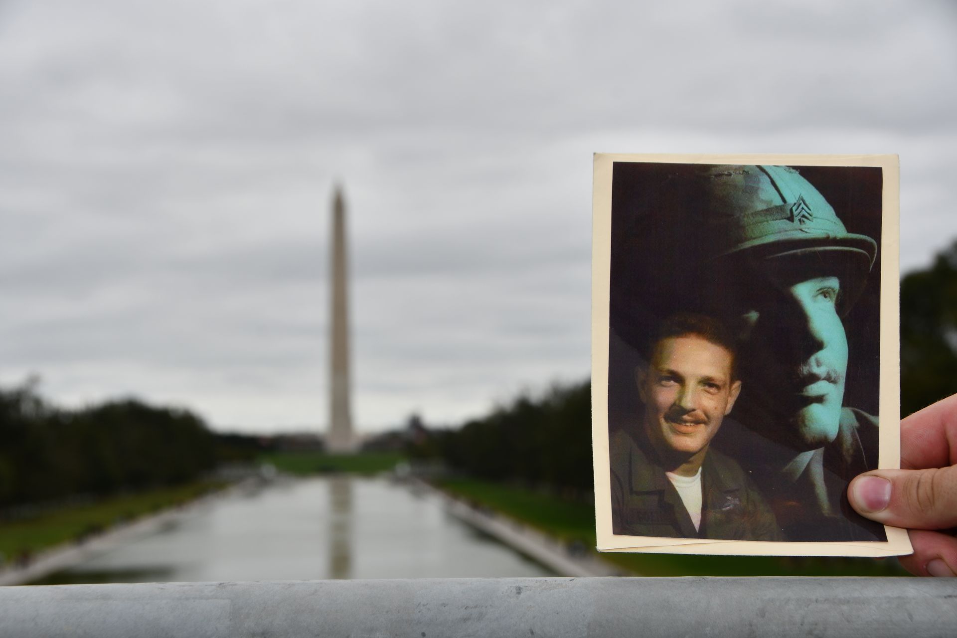 Hand holding photo of two men with Washington Monument in the background.