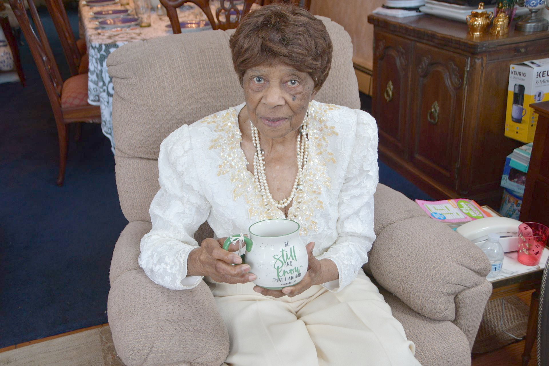 Woman in white top, holding a mug, seated in a recliner.