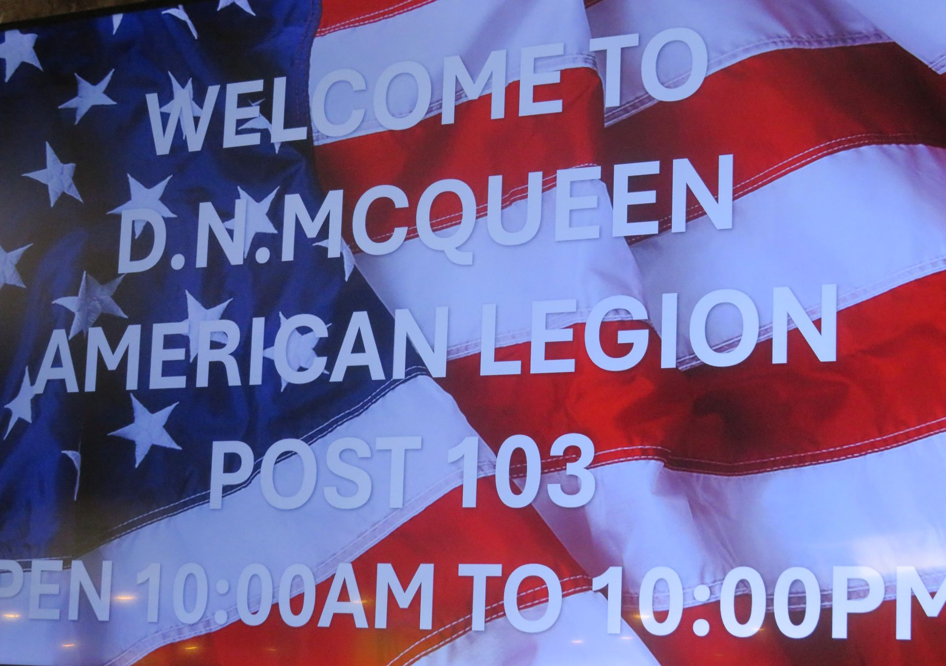 Blue American Legion sign reading “Welcome to D.N. McQueen American Legion Post 103,” with hours listed.