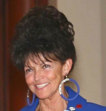 A woman wearing a blue jacket and hoop earrings smiles for the camera