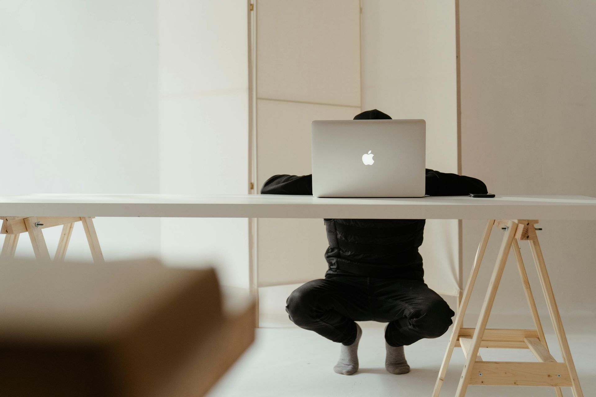 Person kniet hinter einem Macbook in modernem Büro
