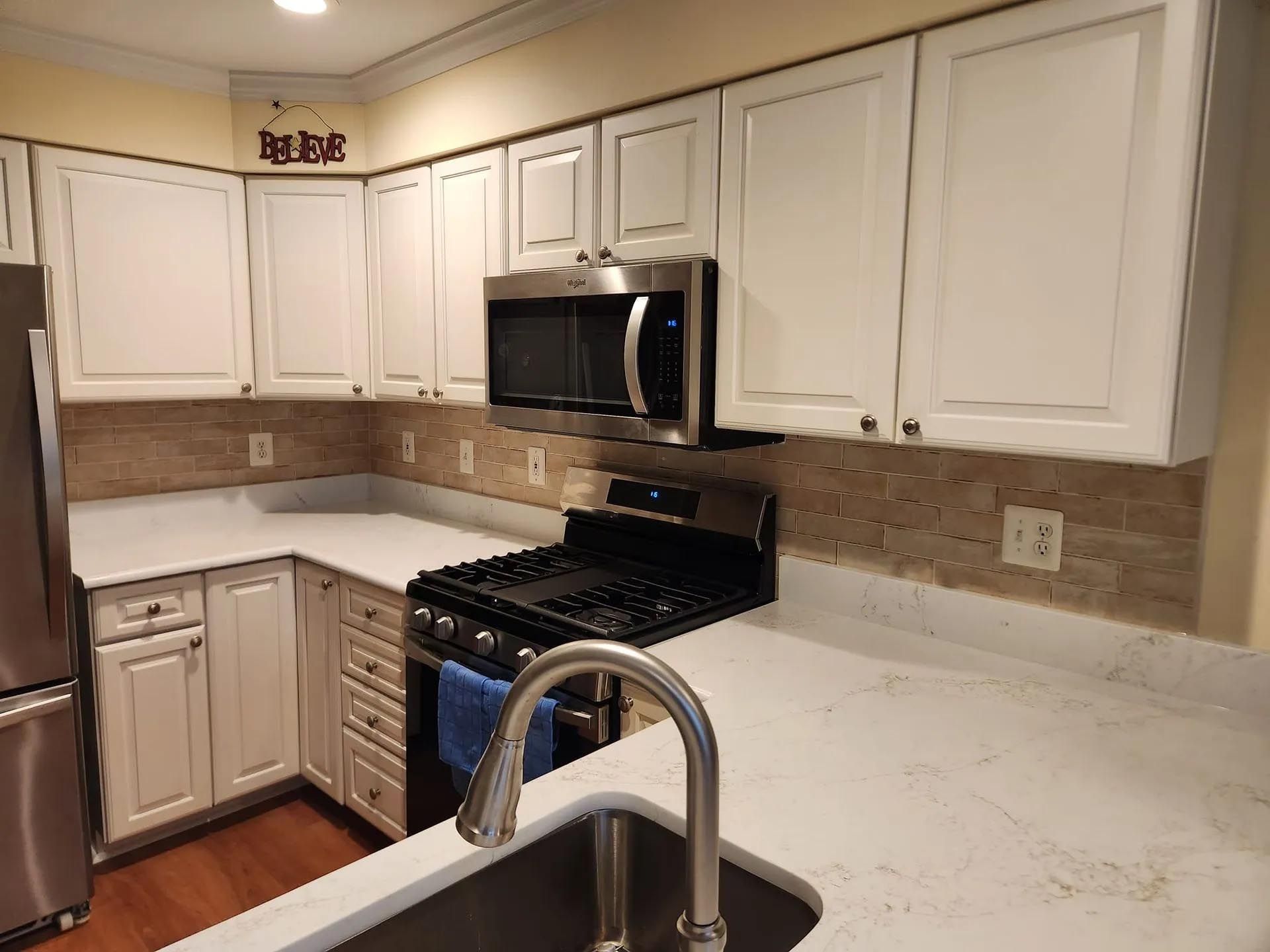 A kitchen with white cabinets , stainless steel appliances and a sink.