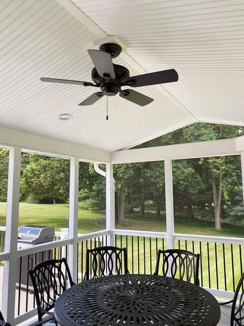 A screened in porch with a table and chairs and a ceiling fan.