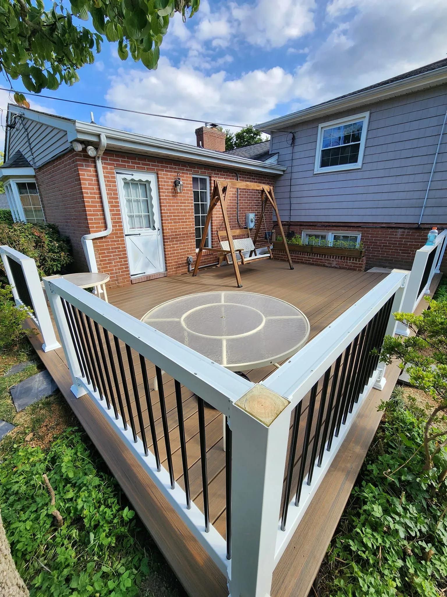 A deck with a swing and a table in the backyard of a house.