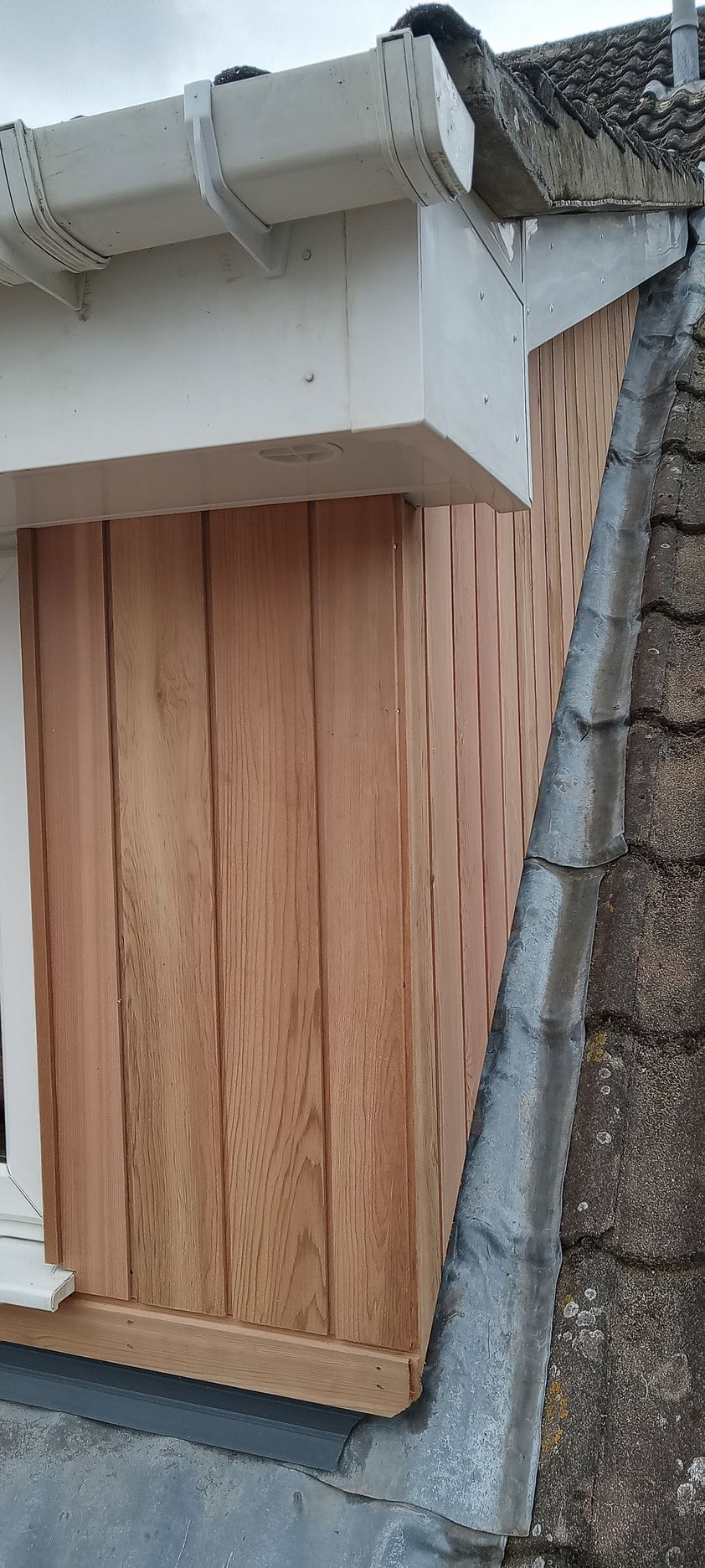 A wooden building with a window and gutter on the side of it.