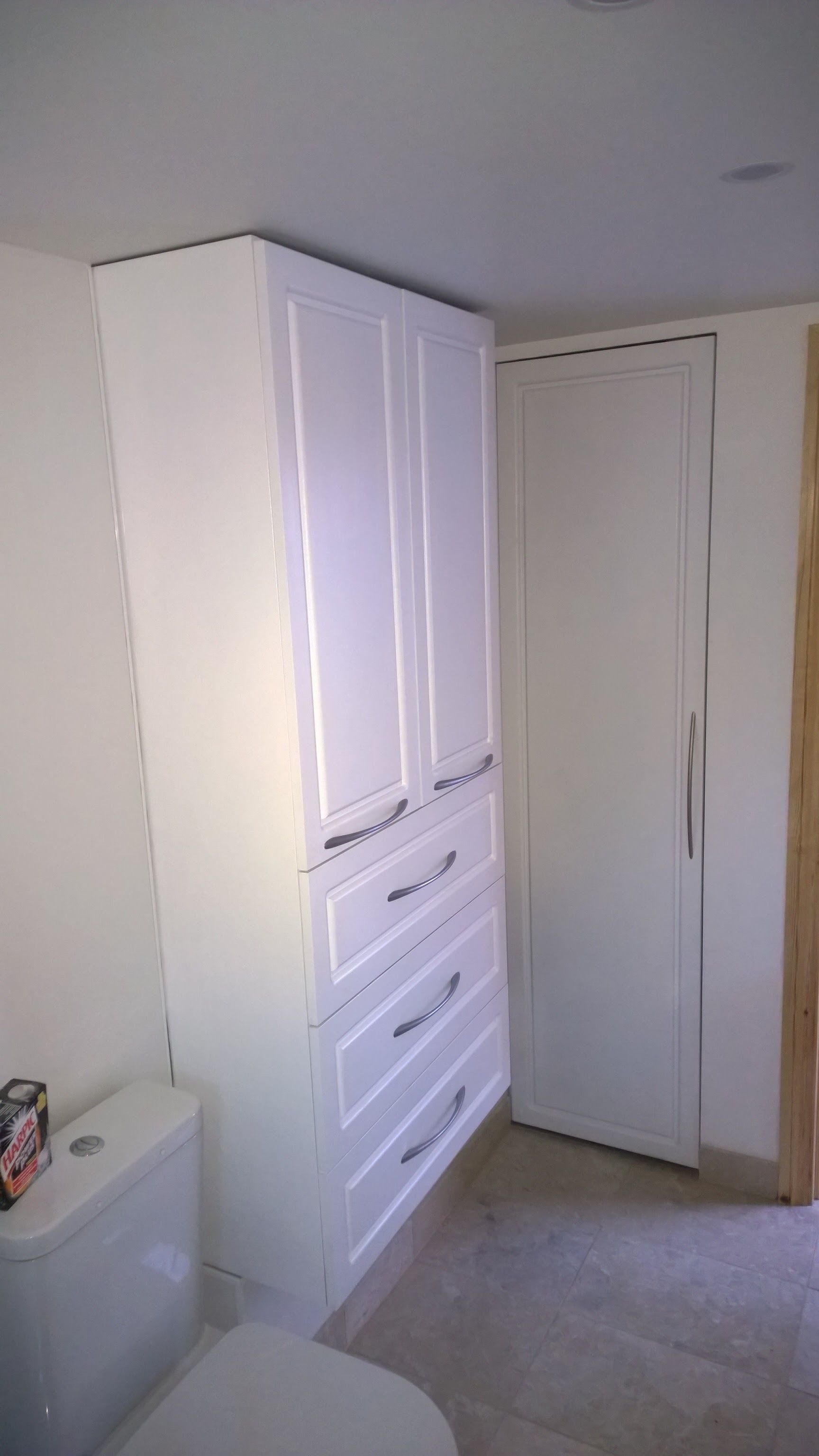 A bathroom with white cabinets , a toilet , and a door.