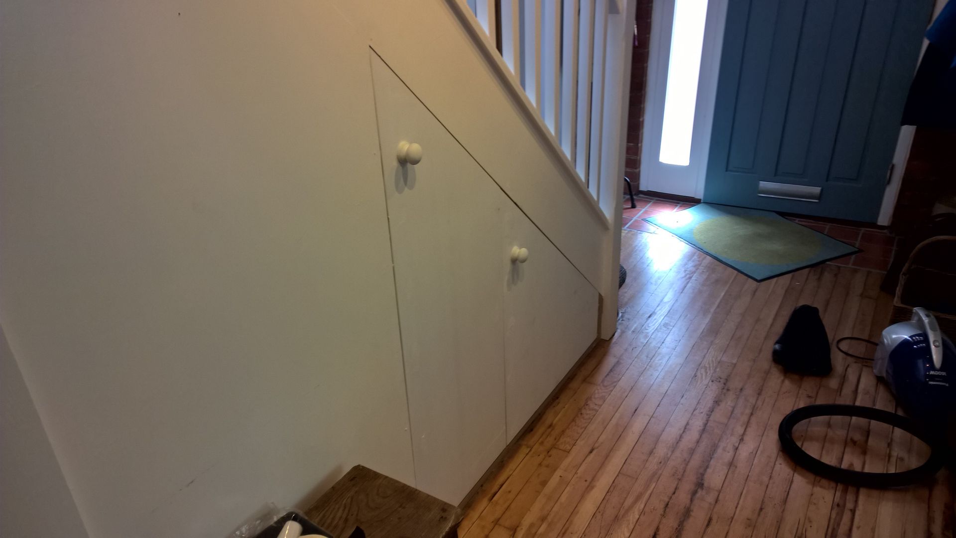 A vacuum cleaner is sitting under a staircase in a hallway.