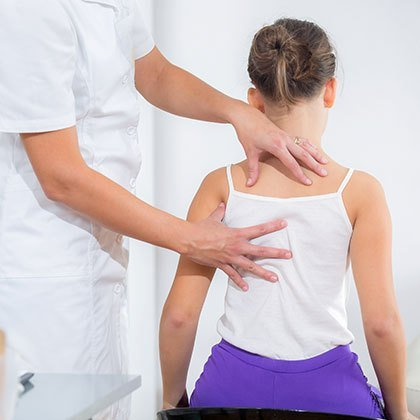 A female therapist's hands on the back of a little girl in a white strappy vest
