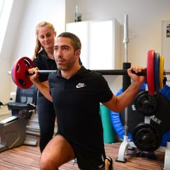 Sporty young man doing squats exercises with the assistance of his sports therapist in the R P Sports Injury clinic.