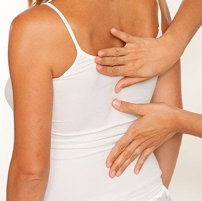 Hands of a therapist on the back of a lady in a white strappy top