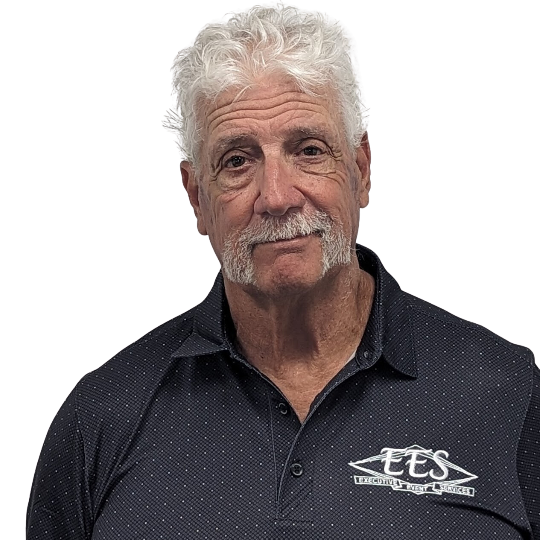 A man with white hair and a beard is wearing a black polo shirt.