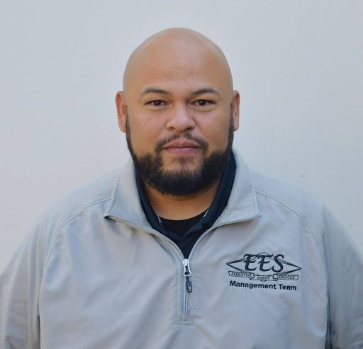 A man with a beard is wearing a white shirt that says ees