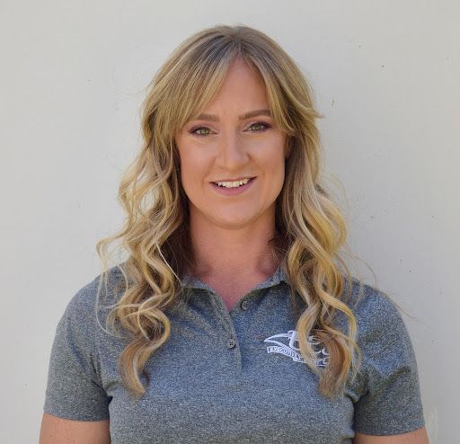 A woman with long blonde hair is wearing a grey polo shirt and smiling.