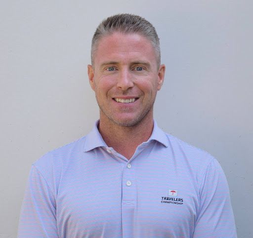 A man is wearing a white polo shirt and smiling.