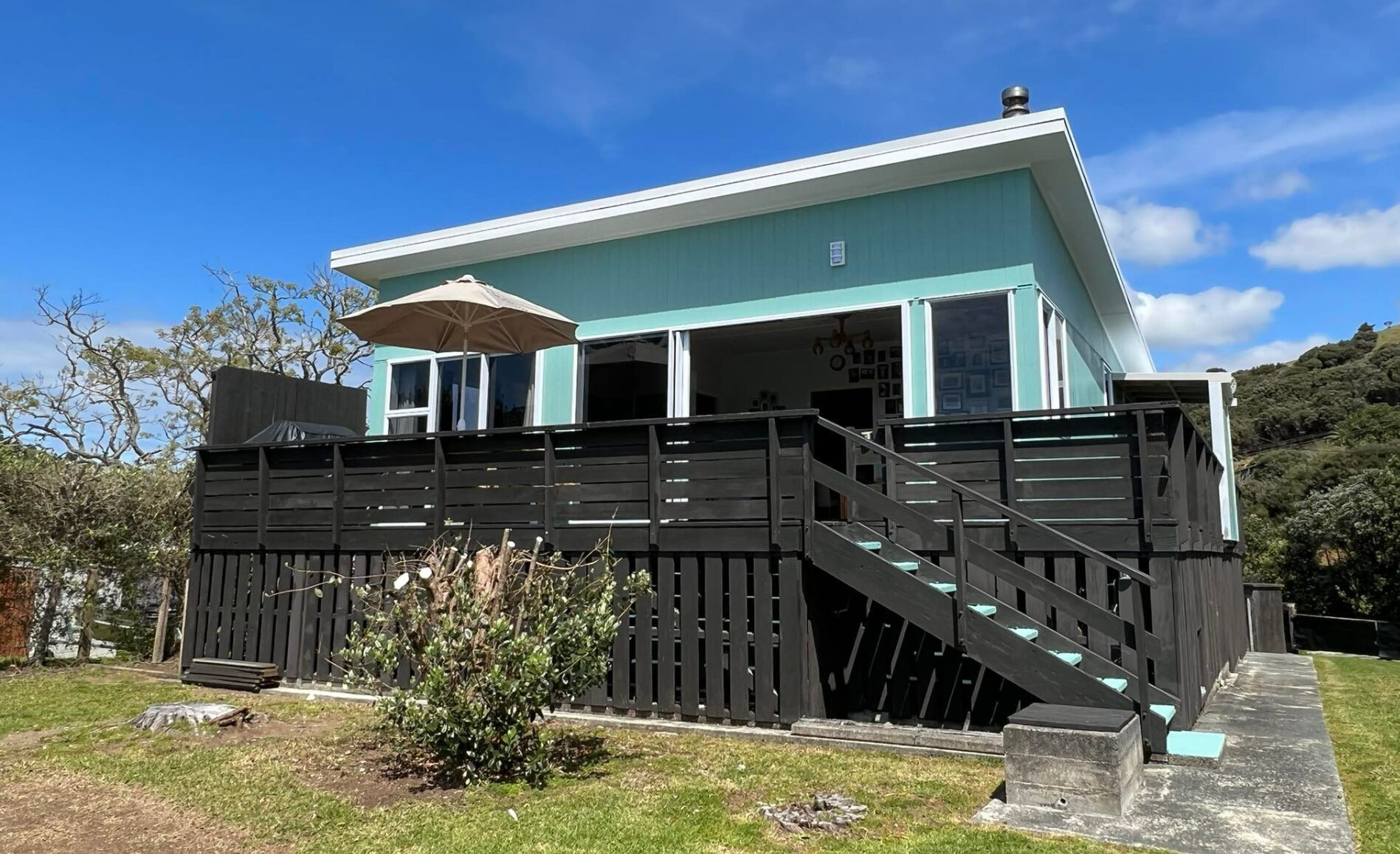 Light blue house with black deck and stairs under a clear blue sky