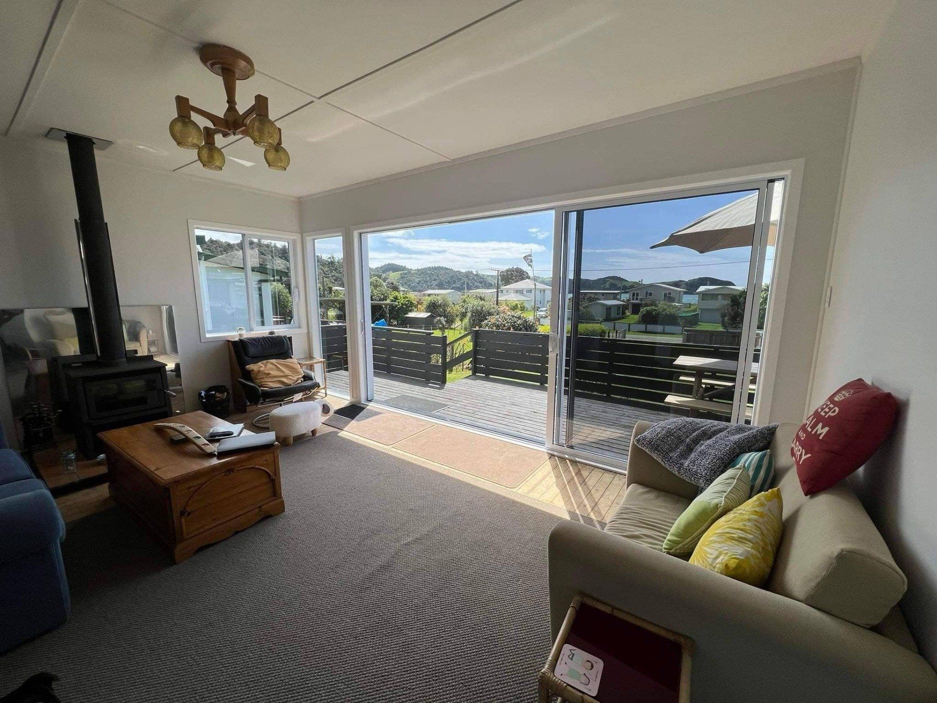 Bright living room with sliding glass doors, patterned carpet, sofa, and a view of rooftops and hills outside