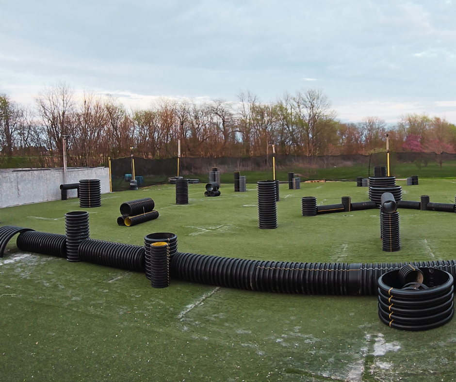 A group of people holding paintball guns posing on a green field inside a building. Most smile at the camera.