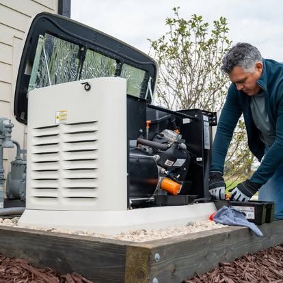 White home generator beside a wooden fence on gravel, with a vented side panel and hose attached