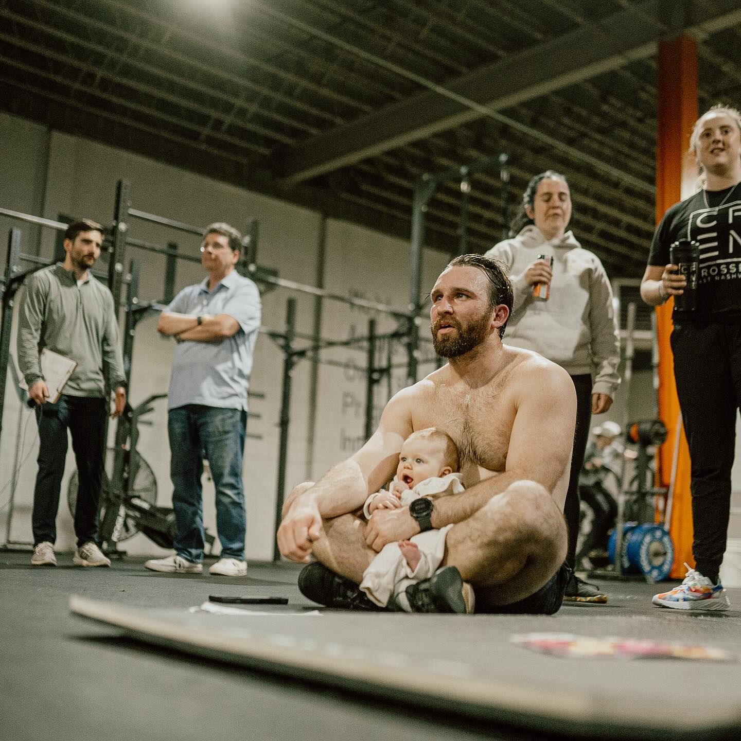 A man is sitting on the floor holding a baby in a gym.